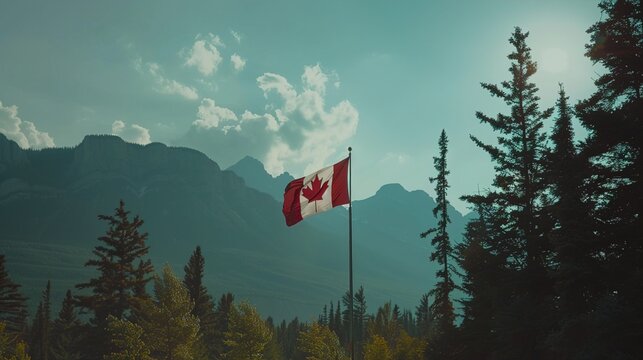 The Canadian flag flying high with a backdrop of mountains and trees.
