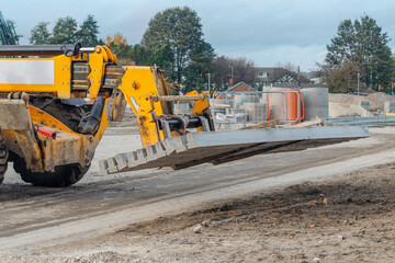 Yellow Excavator Lifting Concrete Slab During Construction Site Work
