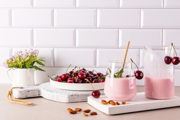 Freshly made cherry smoothie in a large glass glass with eco straw on a wooden board opposite a dish of ripe cherries. Detox. diet.