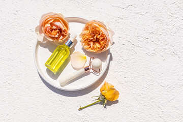 Glass cosmetic bottle with pipette with natural massage oil and roller stone massager on ceramic tea rose tray. top view. Care, beauty.