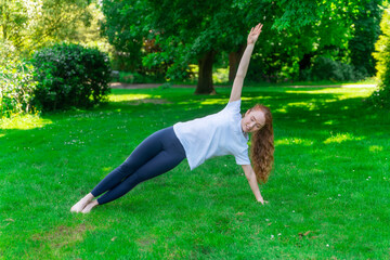 Fototapeta premium Woman Performing Side Plank Exercise On Grass In Park During Sunny Day