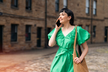 Woman in Green Dress Talking on Phone While Walking on Cobblestone Street