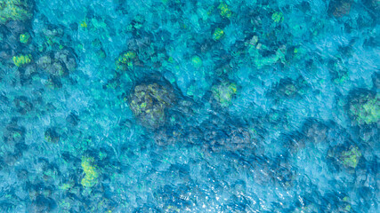 Top view. Summer sea water, blue surface. The water is clear with ripples and sparkles in the sunlight and you can see coral under the sea	