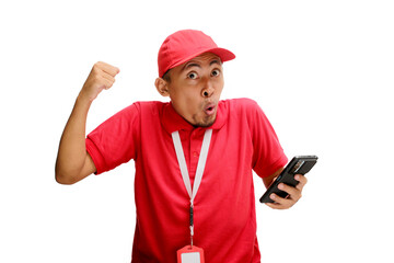 An excited Asian delivery man or courier clenching his fist in a yes gesture, celebrating good news received on his phone. Isolated on a white background