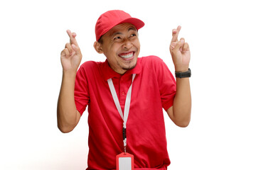 Excited Asian delivery man or courier smiles eagerly while showing a finger crossed gesture,...