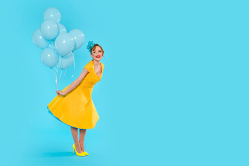 Woman in Yellow Dress Holding Blue Balloons Against Light Blue Background