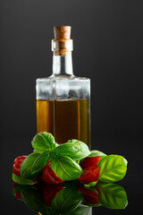 Bottle of olive oil and tomatoes with basil on a black background.