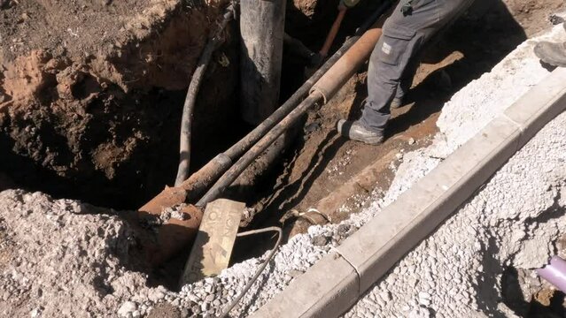 Worker Replacing Underground Cables Near Curb on Sunny Day