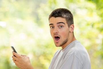 young man with mobile or cell phone outdoors with surprised expression