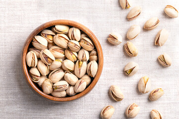 Pistachios in their shells, roasted and salted, in a wooden bowl on linen fabric. Crunchy roasted fruits of Pistacia vera, with opened shells and seeds within. Ready-to-eat snack food. Close-up. Photo