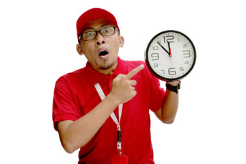 Asian delivery man or courier looks surprised as he points at a clock in his hand, isolated on a...
