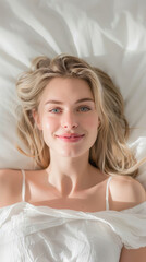 Fototapeta premium Beautiful smiling young blonde female model with long hair, natural skin care and perfect smooth skin relaxing lying on soft white bed while looking up