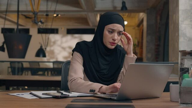 Displeased sad worker muslim islamic businesswoman in hijab upset online project mistake Arabian man businessman boss coach come help trainee solve problem excited happy woman working laptop in office