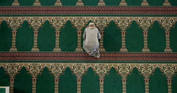 Muslim woman, above and praying at mosque for salah, duah or faith on traditional carpet or mat. Top view of holy female person or hijab in islamic prayer for Allah, worship god or religion on floor
