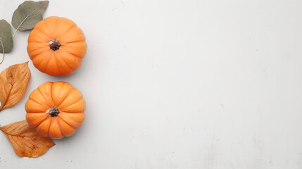 Two small orange pumpkins and fall leaves are arranged on a white background, creating a minimalist and festive Halloween backdrop