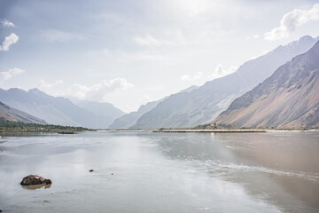 Wide Panj River in the valley of the Wakhan corridor against the backdrop of mountain ranges and peaks on the Pamir Highway in the mountains of Tajikistan in the Tien Shan, panoramic landscape