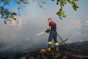 Fire in the field near the city. Firefighter extinguishes a fire.