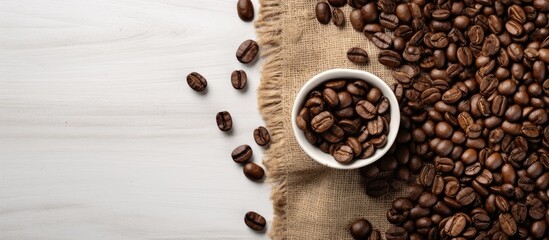 On a white table background, there is a top-down view of roasted coffee beans next to a sack, with room for additional content in the image.