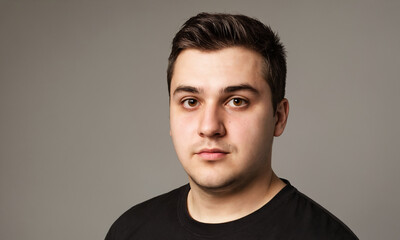 Obraz premium Portrait of a young man with dark hair in a black t-shirt against a grey background