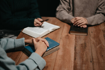Obraz premium Group of Christians sit together and pray around a wooden table with blurred open Bible pages in their homeroom.