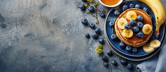 Top view of pancakes with blueberries, banana, and honey on a concrete surface, providing ample copy space image for text.