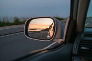 Sunset in the side mirror. View from the the drivers seat while driving the car in the evening.