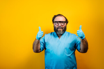 The doctor in a blue coat on a yellow background gestures with latex gloves.