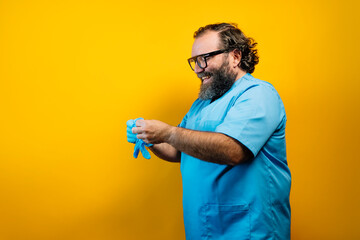 The doctor in a blue coat on a yellow background gestures with latex gloves.