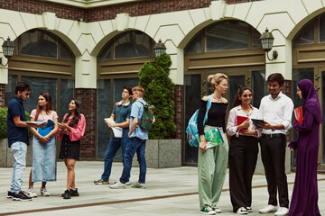 Mixed group of friends,. multiracial people, boys and girls standing outdoors and preparing for their final exams in a campus garden. Concept of education, university, multicultural students, unity