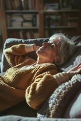 A woman is laying on a couch with a blanket and a pillow. She is smiling and she is relaxed