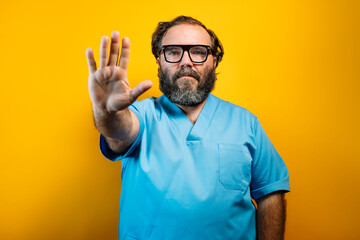 The doctor in a blue coat on a yellow background makes a STOP gesture.