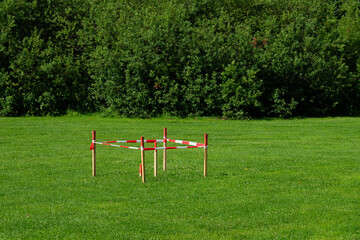 Fototapeta premium A square, constructed from red and white tape, stands alone in a vibrant green field. 
