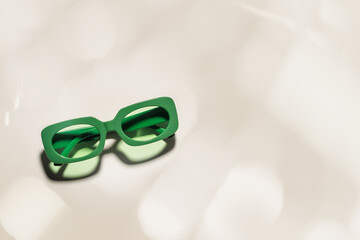 Stylish green colored sunglasses with sunshine on beige background, copy space, shadow and glare...