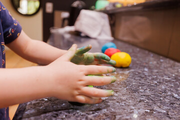 Close up of child's hands kneading green food colouring into playdough mixture