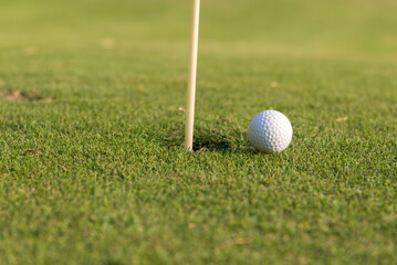 Close-up of golf ball on grass golf course and sunrise background.