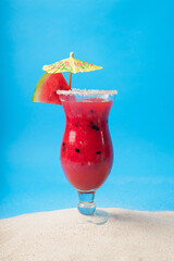 Watermelon juice on sea sand with blue background. Summer background.