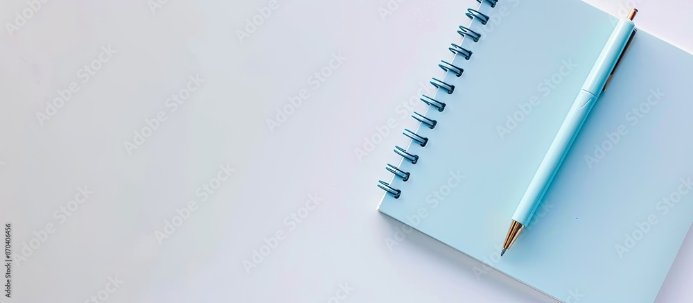 Poster top view of a light blue spiral notepad with a pen on a white desk background for your design, featu