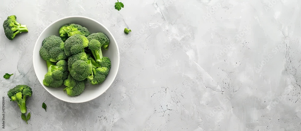 Poster top-down view of a bowl of fresh broccoli on a light grey table with ample space for text alongside 