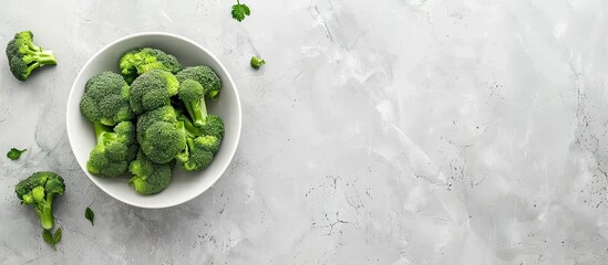 Top-down view of a bowl of fresh broccoli on a light grey table with ample space for text alongside the copy space image.