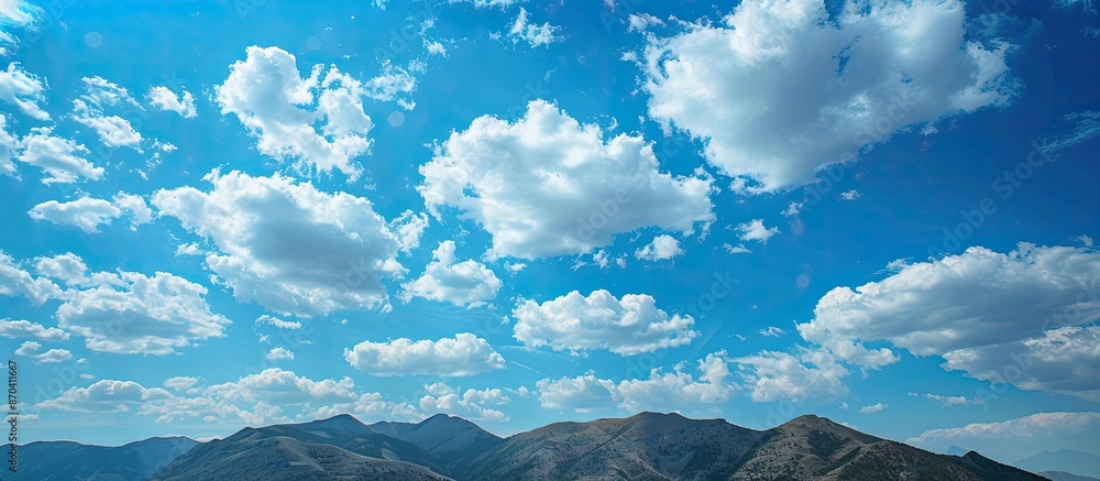 Poster scenic mountain range set against a backdrop of a clear blue sky with scattered clouds, offering a p