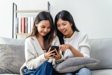Two women sitting on a couch, using and looking at a cell phone