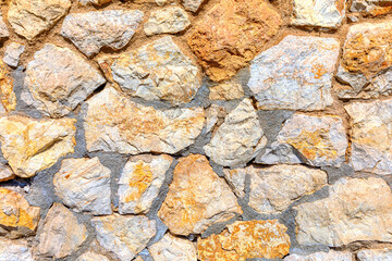 Wall made of stone with a lot of texture. The wall is made of many different sized rocks and has a rough, uneven surface. The wall appears to be old and has a rustic