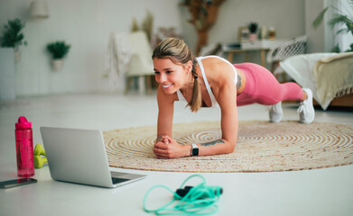 Smiling sporty woman blogger in sportswear shooting video online lessons on laptop and doing...