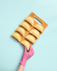A baker wearing a rubber glove arranges raw samosas on the table. These are frozen ready-to-cook traditional Central Asian delicacies.