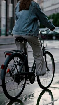 Back view of the girl in safety helmet riding bicycle in rainy evening city
