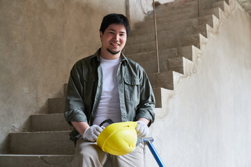 Portrait of smiling young male bricklayer leaning on incomplete staircase in corridor at...