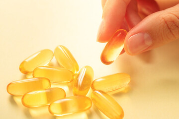 One capsule with omega 3 in hand next to a handful of the same capsules with fish oil.
