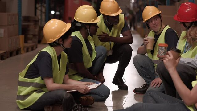 Inclusive, multiracial warehouse team, including a worker with Down syndrome, enjoying a coffee break together. Diverse warehouse team taking a coffee break
