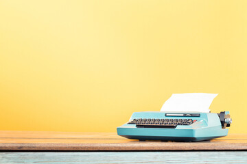 Retro typewriter from circa 1980s with sheet of paper on wooden desk front yellow wall background....