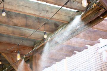 Water spray system for cooling the terrace on a hot summer day. Fogging system, high pressure water spray. Wooden ceiling in loft style.
